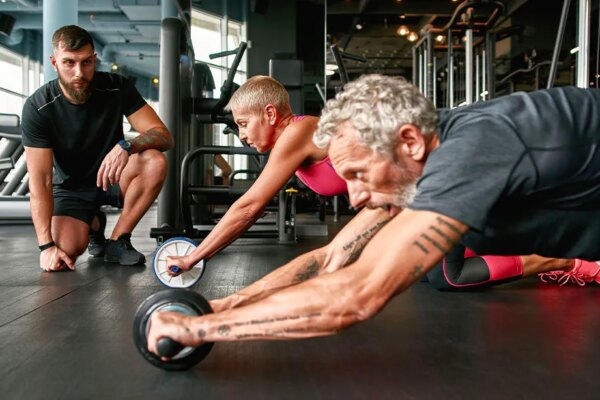Elderly couple performing an ab rollout workout with a trainer looking on