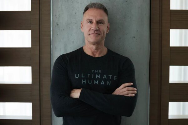 Gary Brecka wearing a black ultimate human shirt leaning against a wall