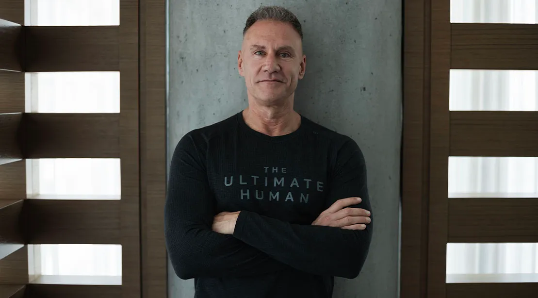 Gary Brecka wearing a black ultimate human shirt leaning against a wall