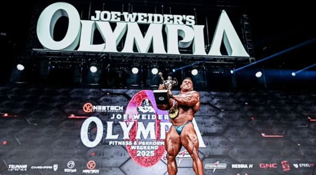 Derek Lunsford holding up the Sandow Trophy after winning the 2025 Olympia bodybuidling competition.webp